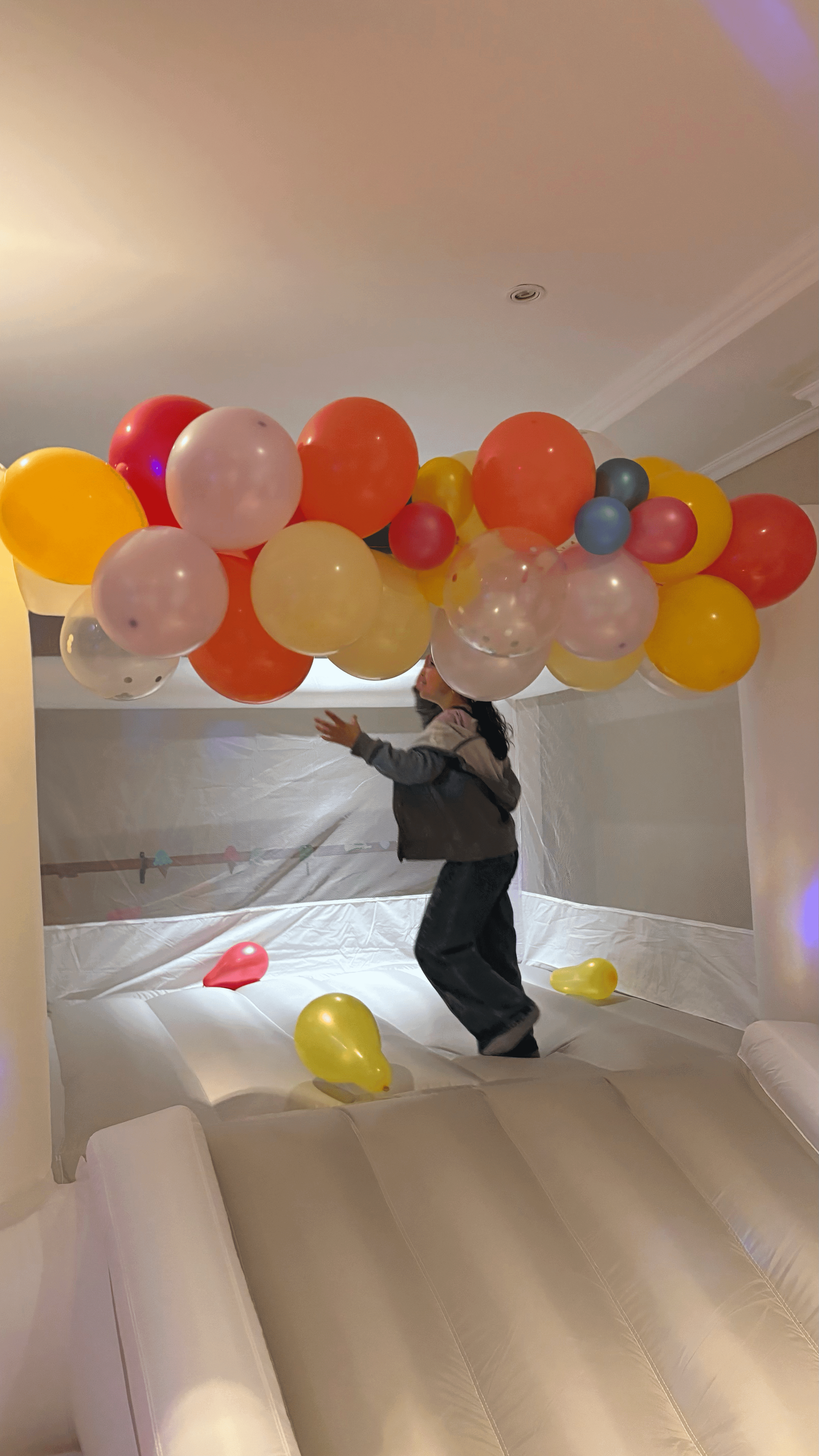 Niña saltando en un inflable blanco con guirnaldas de globos.