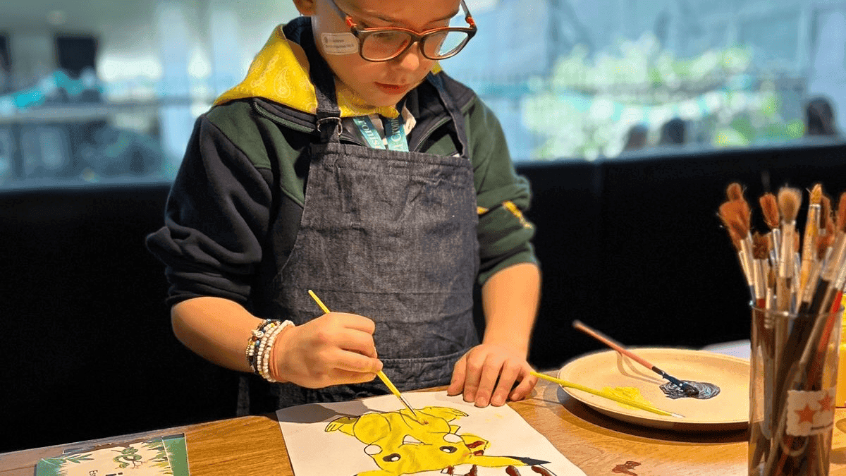 Niño con un delantal pintando una figura de color amarillo.