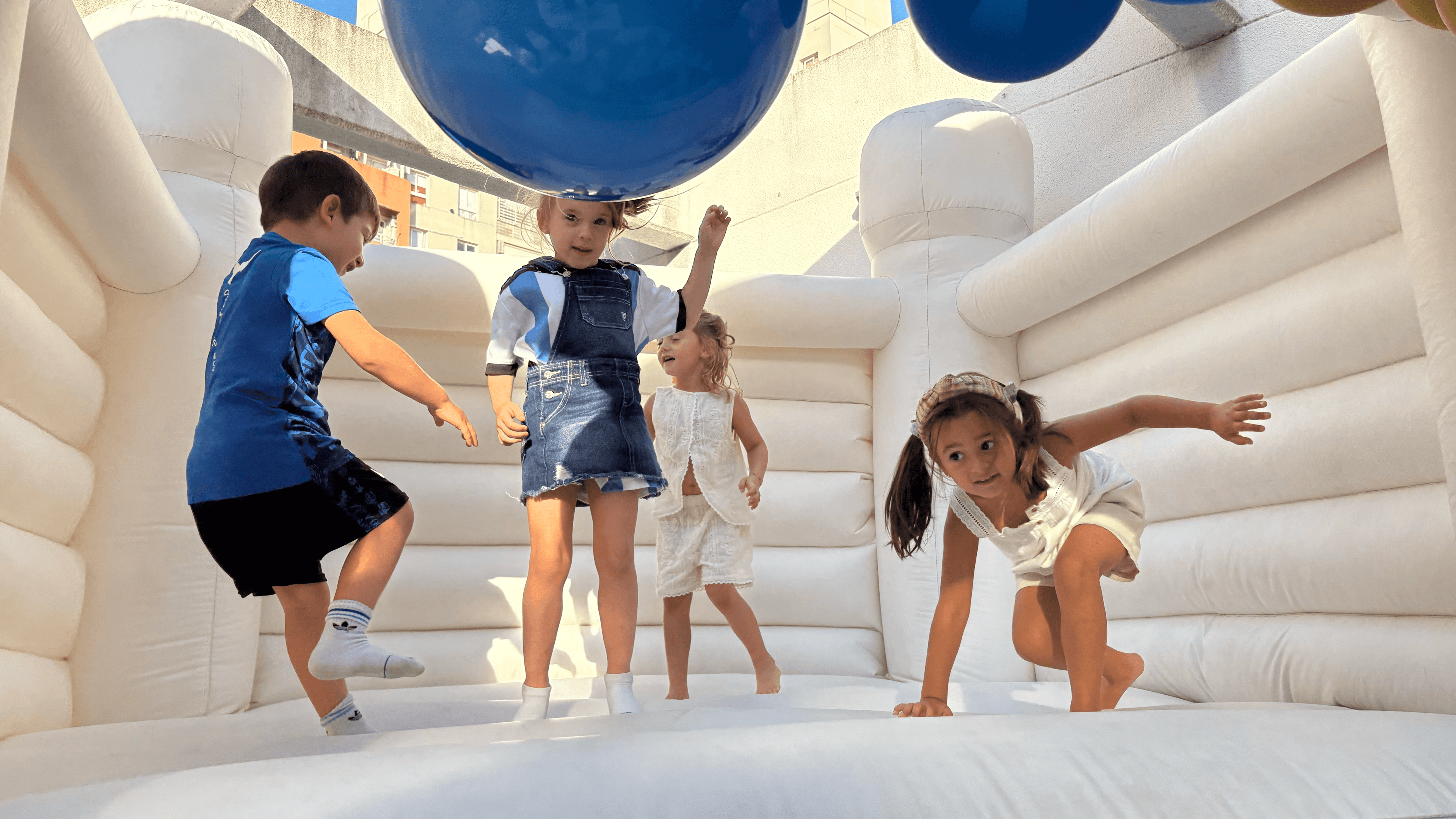 Grupo de niños saltando en un inflable color blanco con una guirnalda de globos encima color azul oscuro.