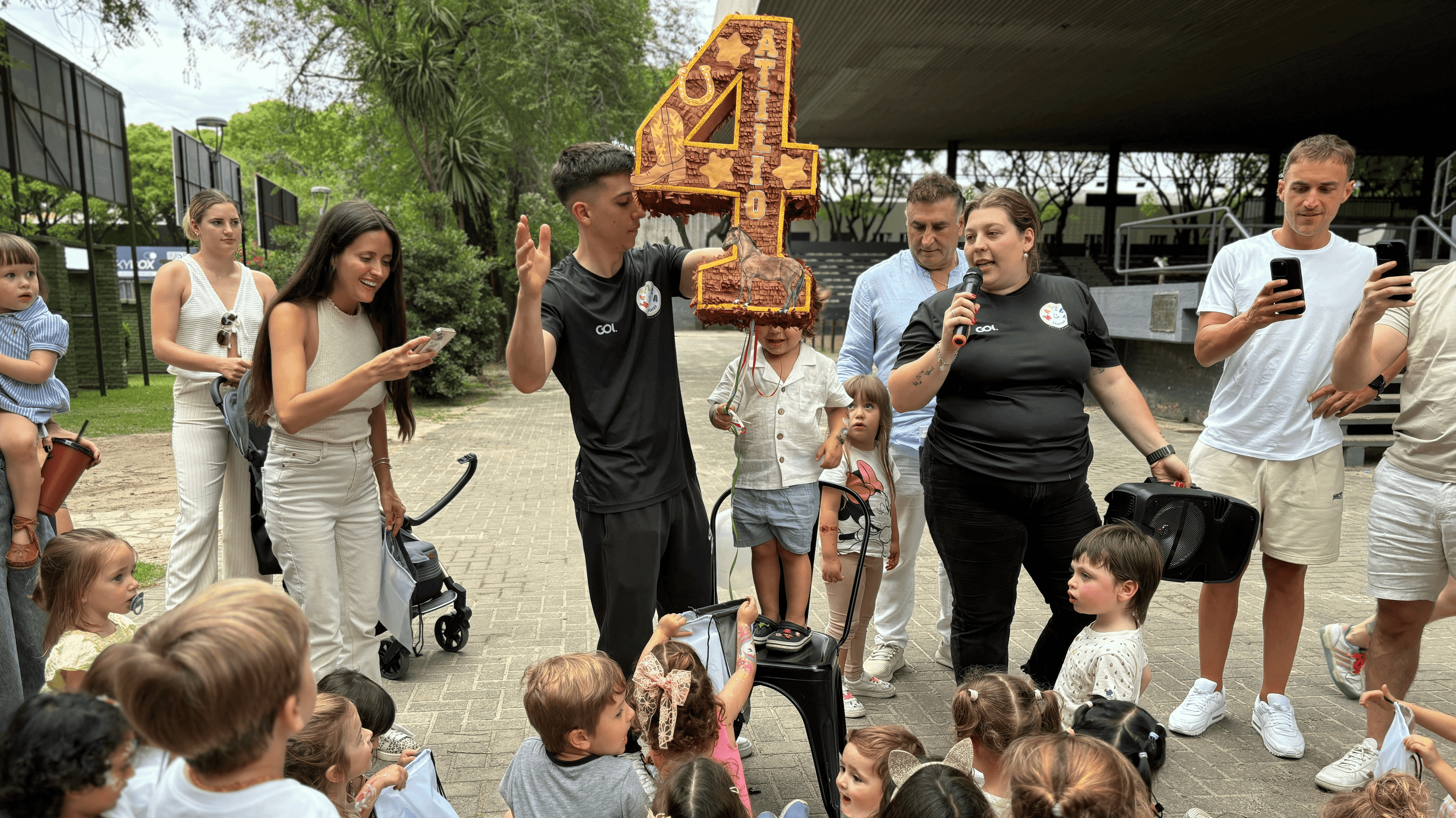Grupo de adultos y niños recogiendo caramelos de una piñata color naranja y marrón con forma de número cuatro.