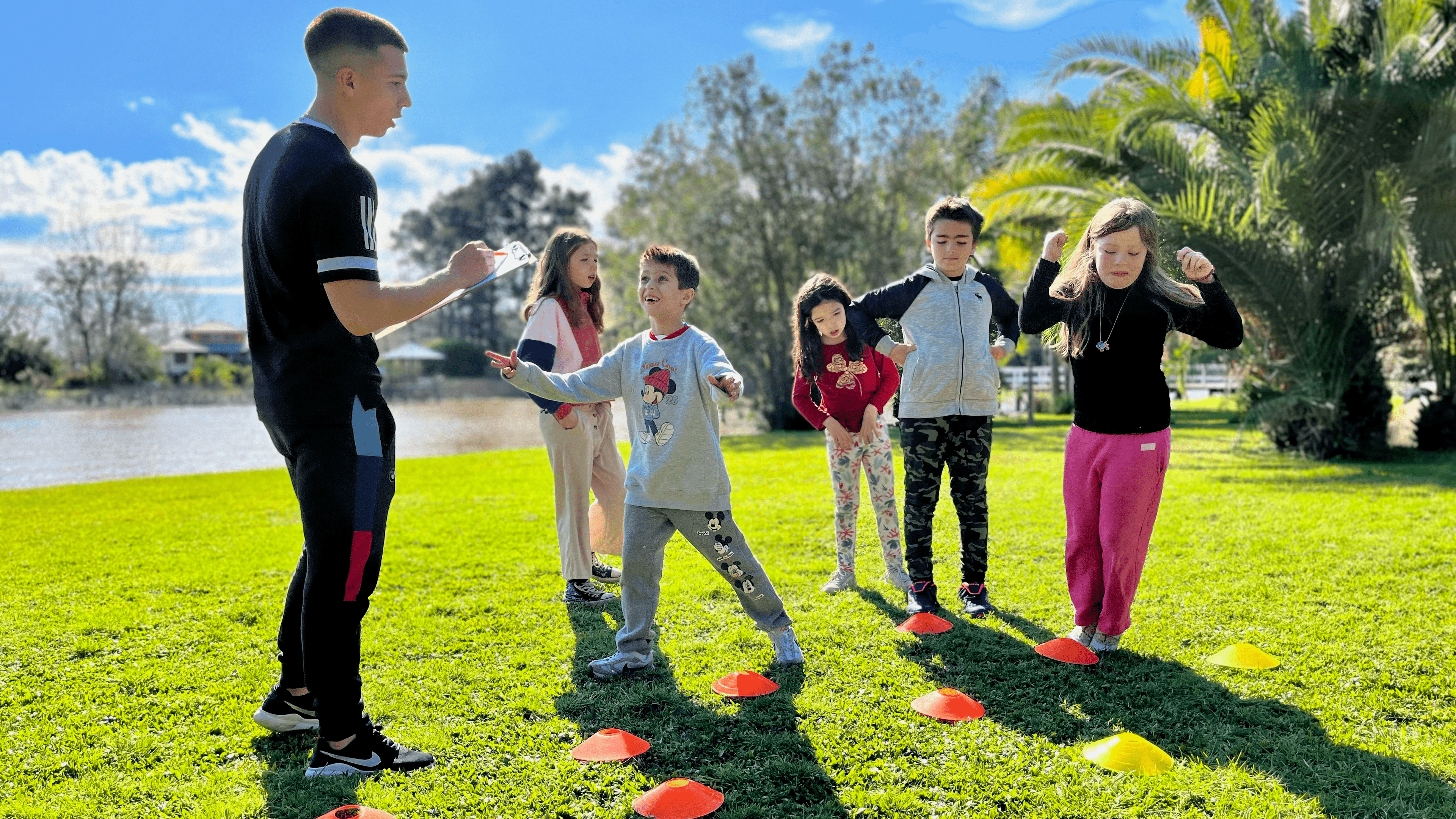 Grupo de niños jugando y escuchando al animador de Matica Eventos en una actividad deportiva que incluye conos.